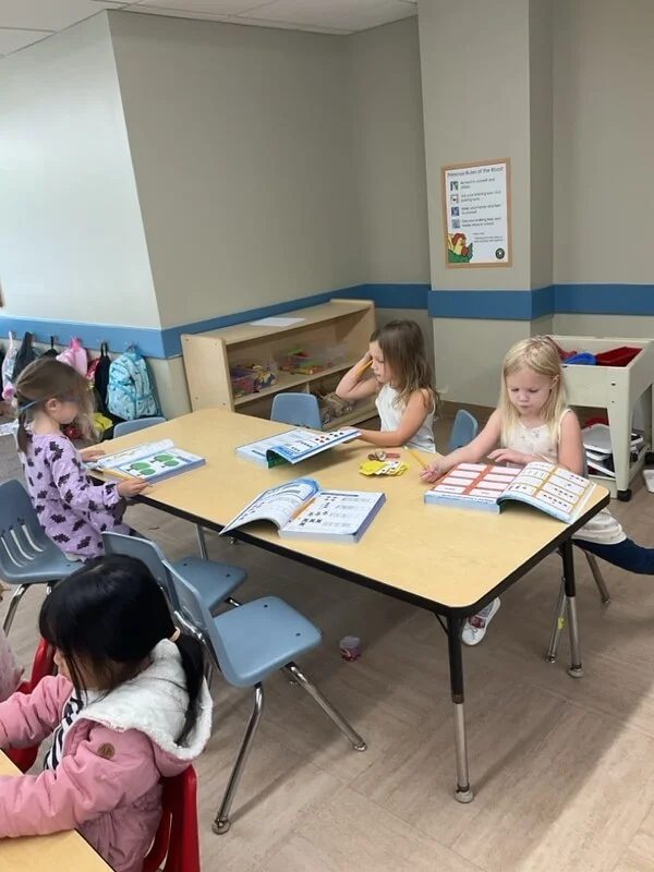 kindergarten children work on math and literacy in their workbooks