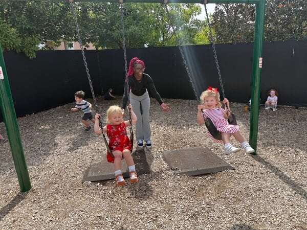 preschool children are pushed on the swing during thumbs up outdoor play