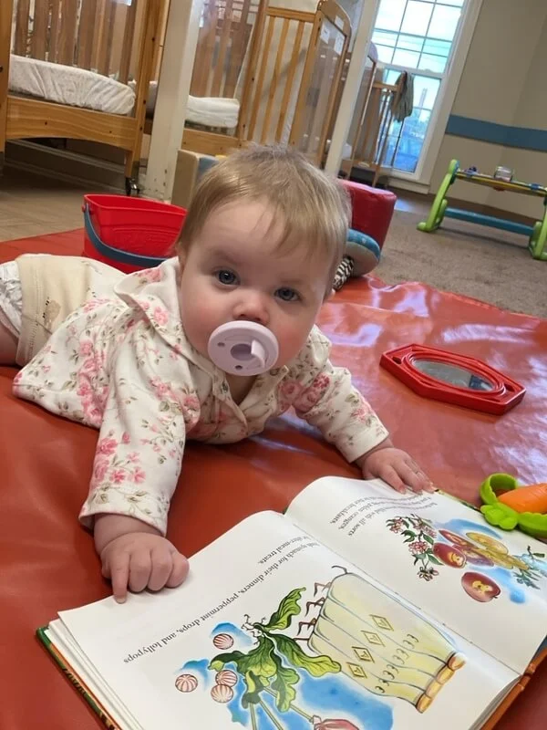 infants spend time on the floor with their teachers surrounded by educational toys and books