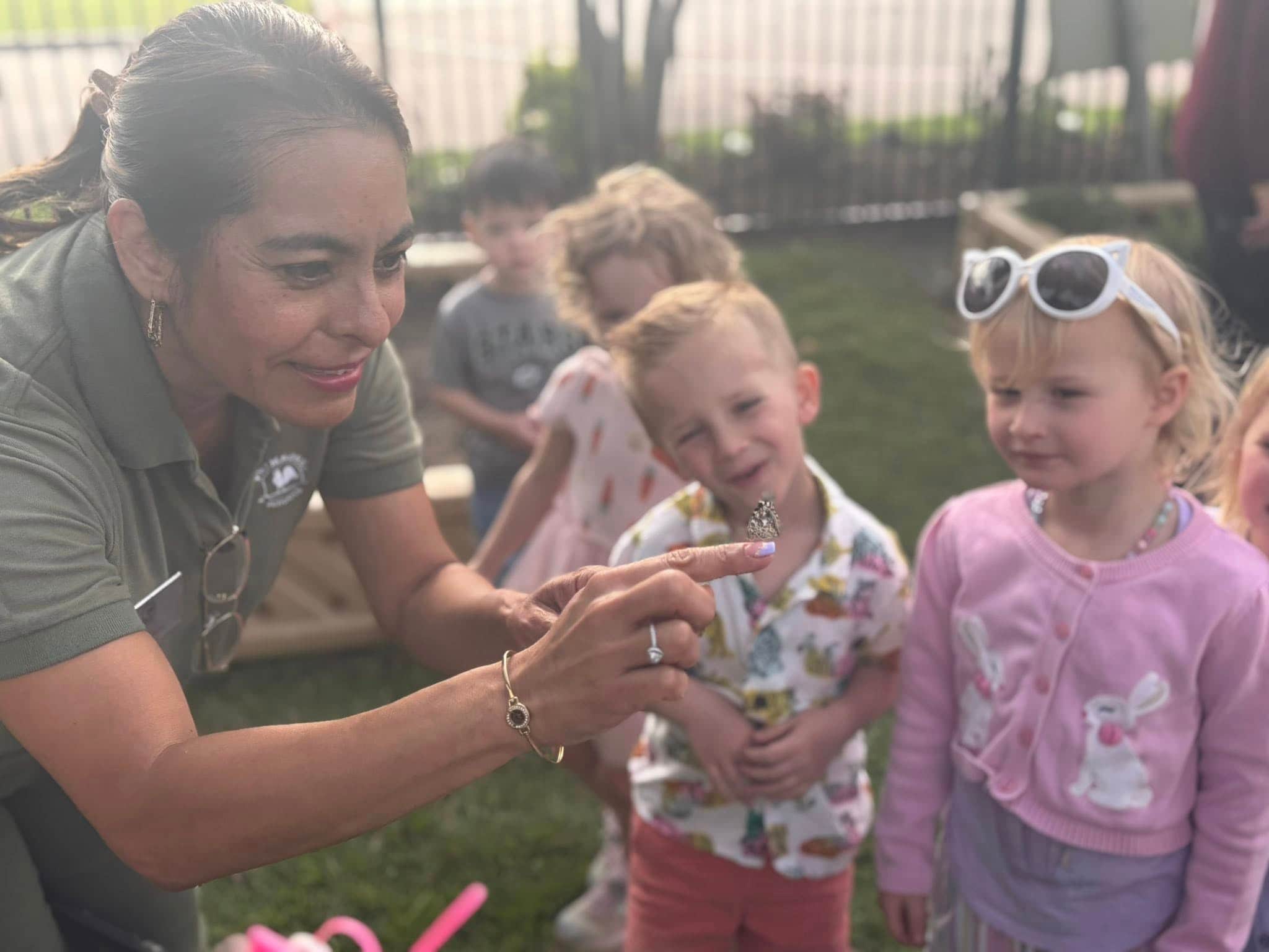 children on a playground observing a teacher holding a butterfly