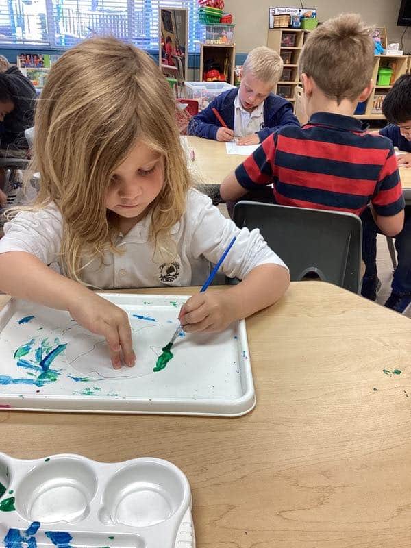 children in school uniforms sitting at tables painting