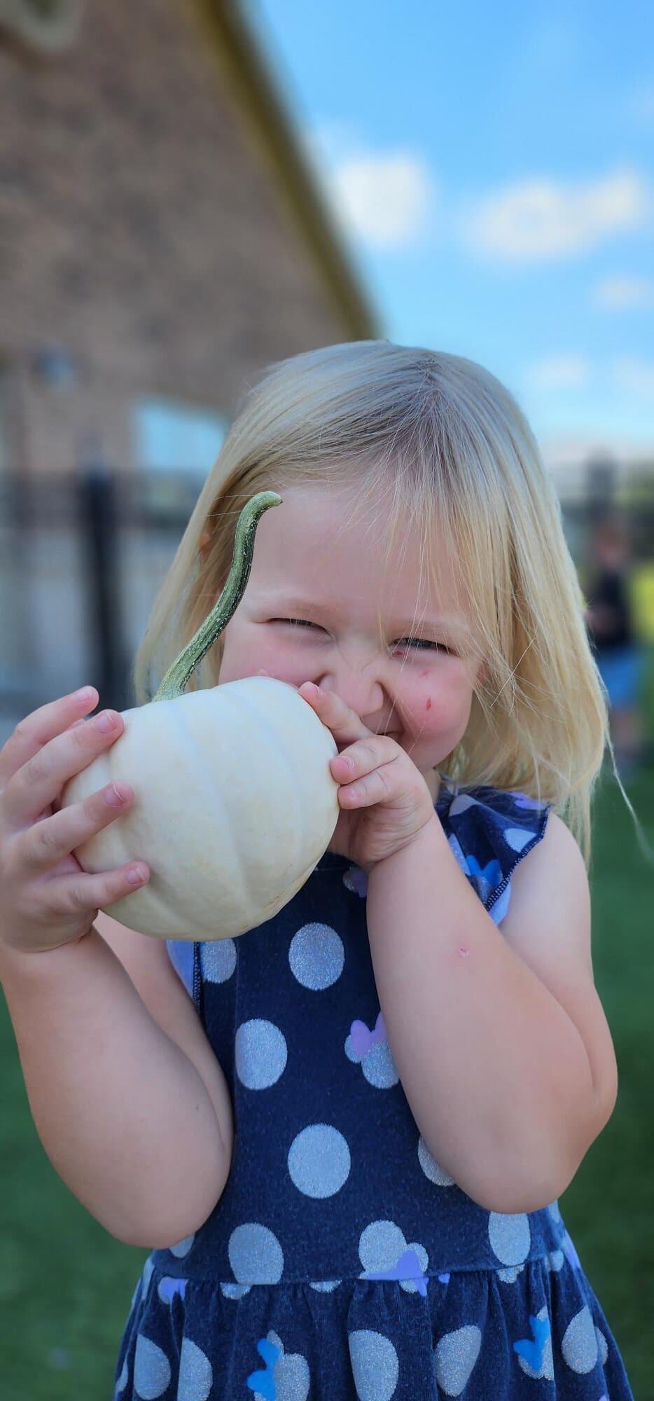Child holding a pumpkin in the school garden during hands-on learning at the best preschool in Alliance. 
