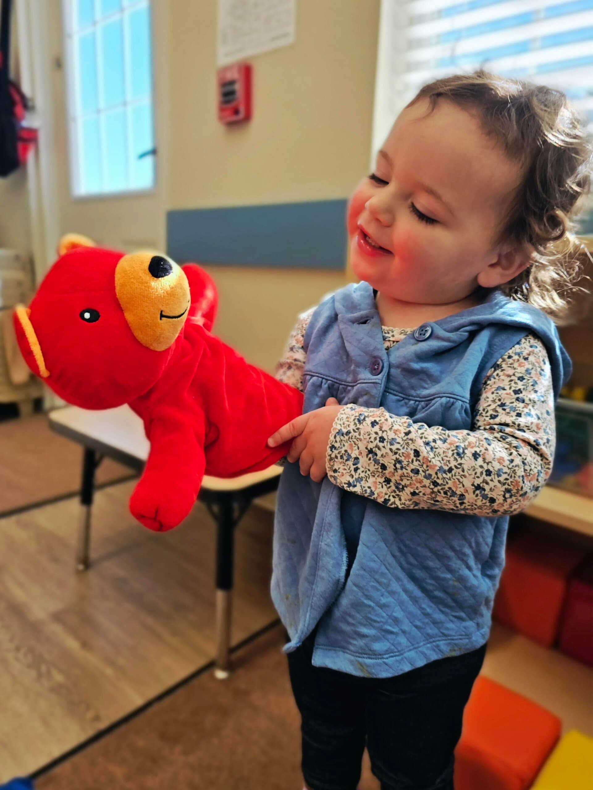 Toddler girl delighting in imaginative play by putting a puppet on her hand at Primrose School at Heritage in Keller, TX.