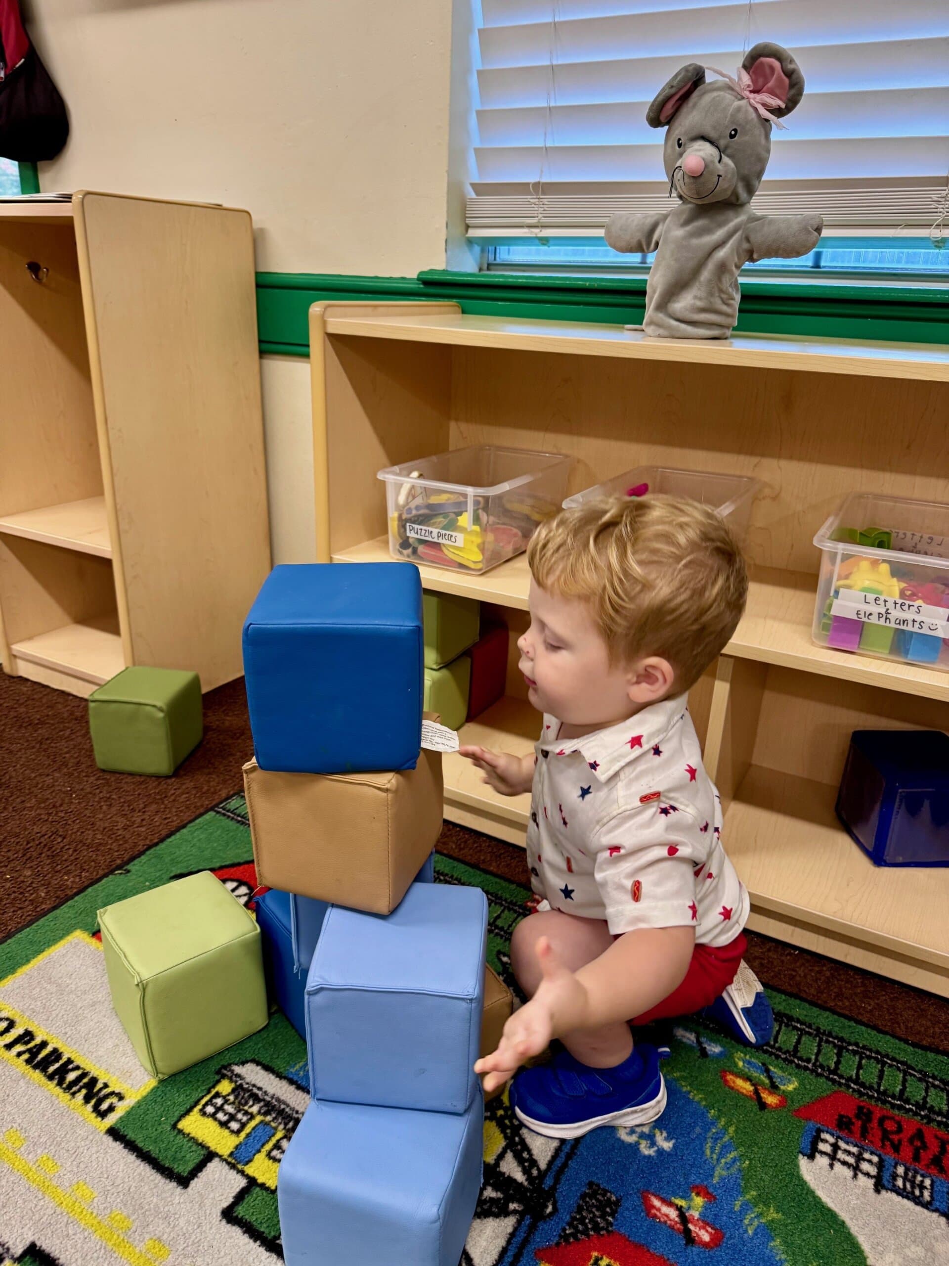 Toddler building a tower with large soft blocks, developing coordination, problem-solving, and spatial awareness through constructive play