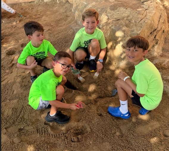 School aged boys on a field trip participating in a Dino Dig activity wearing a Summer Explorers school shirt 