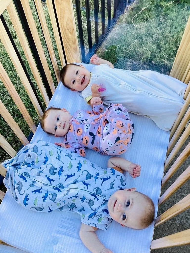 three babies riding in a crib together smiling