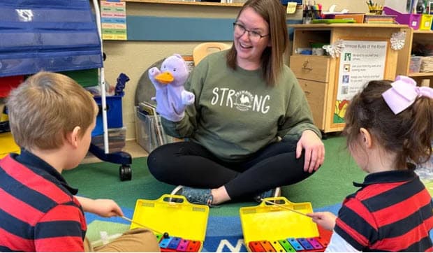 Teacher Leta leading music and puppet play with xylophones on the classroom floor at Primrose School of Eagan in Eagan, MN