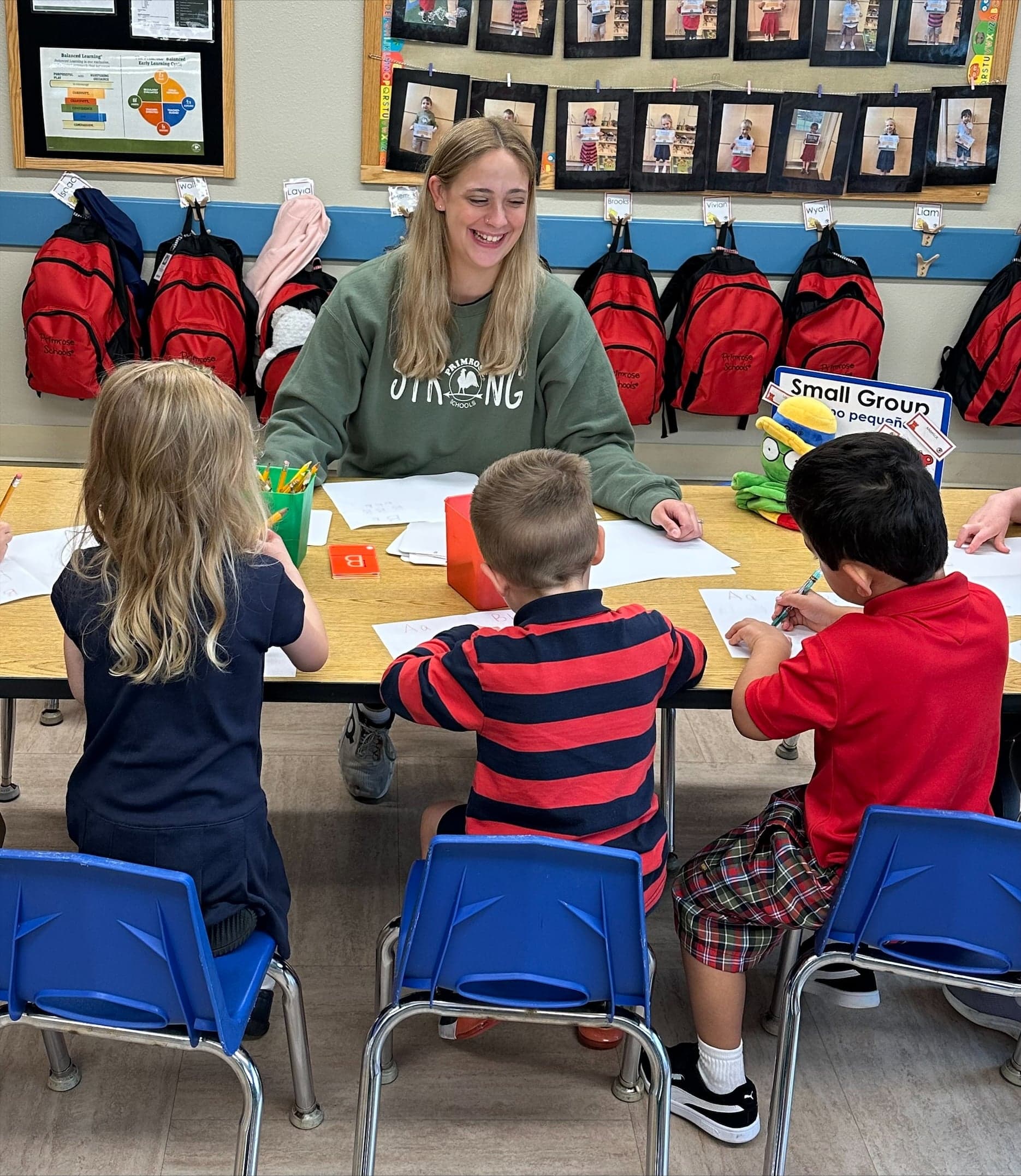 Preschool teacher guiding three students during a writing table lesson at Primrose School of Eagan preschool in Eagan, MN