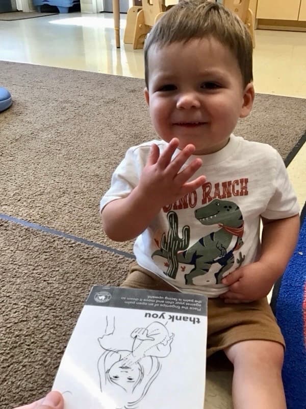 Toddler boy signing thank you with a sign language card of thank you in front of him