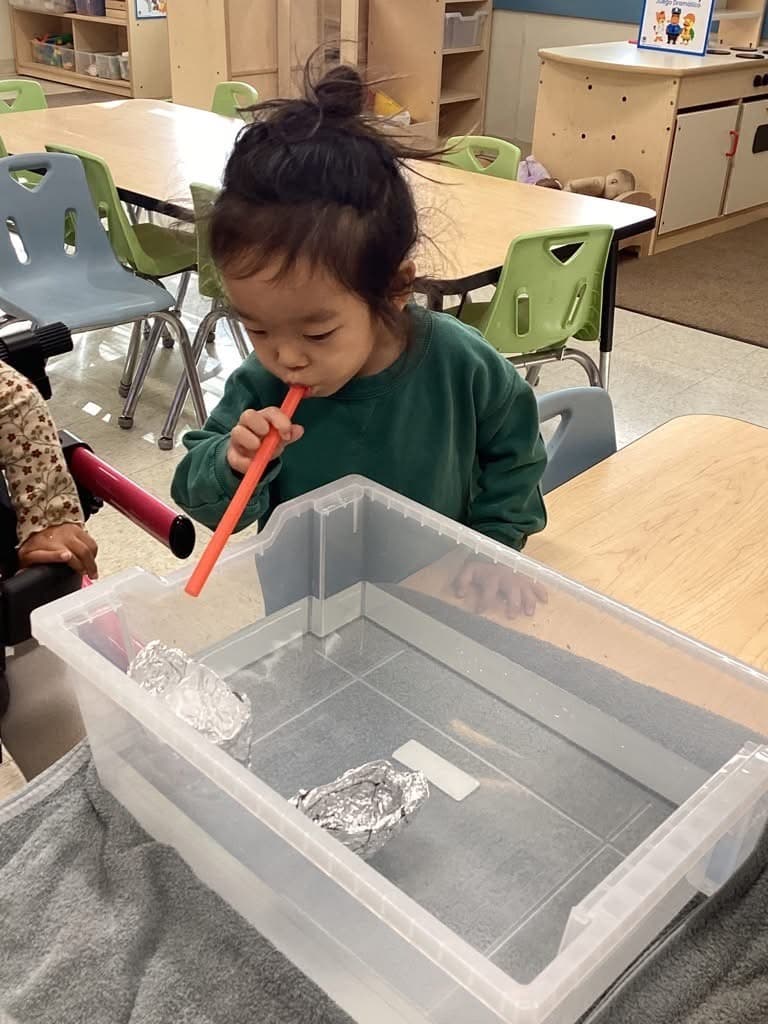 little boy blowing through a straw to move an aluminum boat in water. 