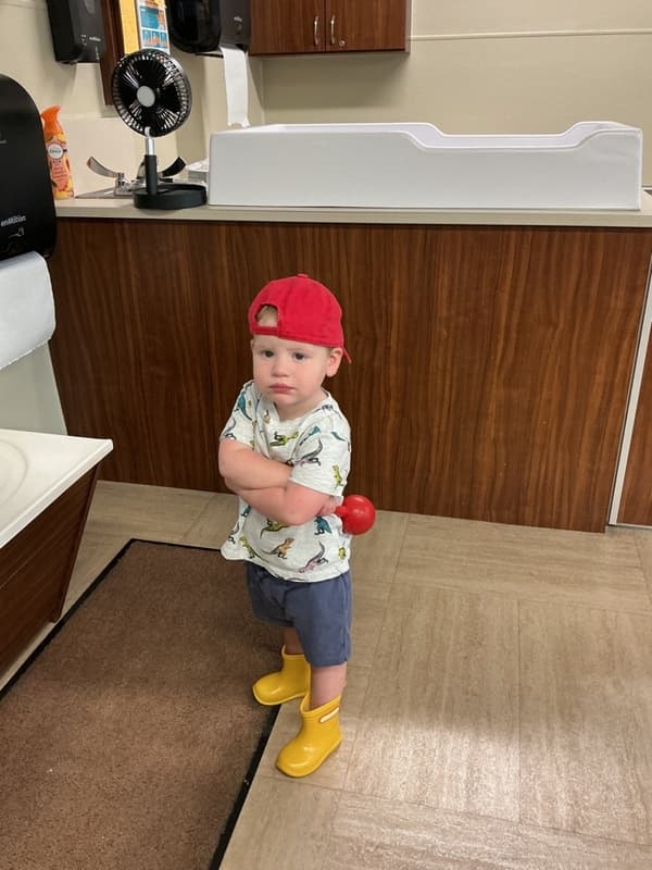 child in red hat, yellow rain boots, and standing with arms crossed