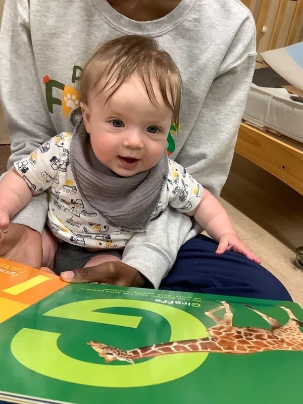 Infant reading a book with their teacher