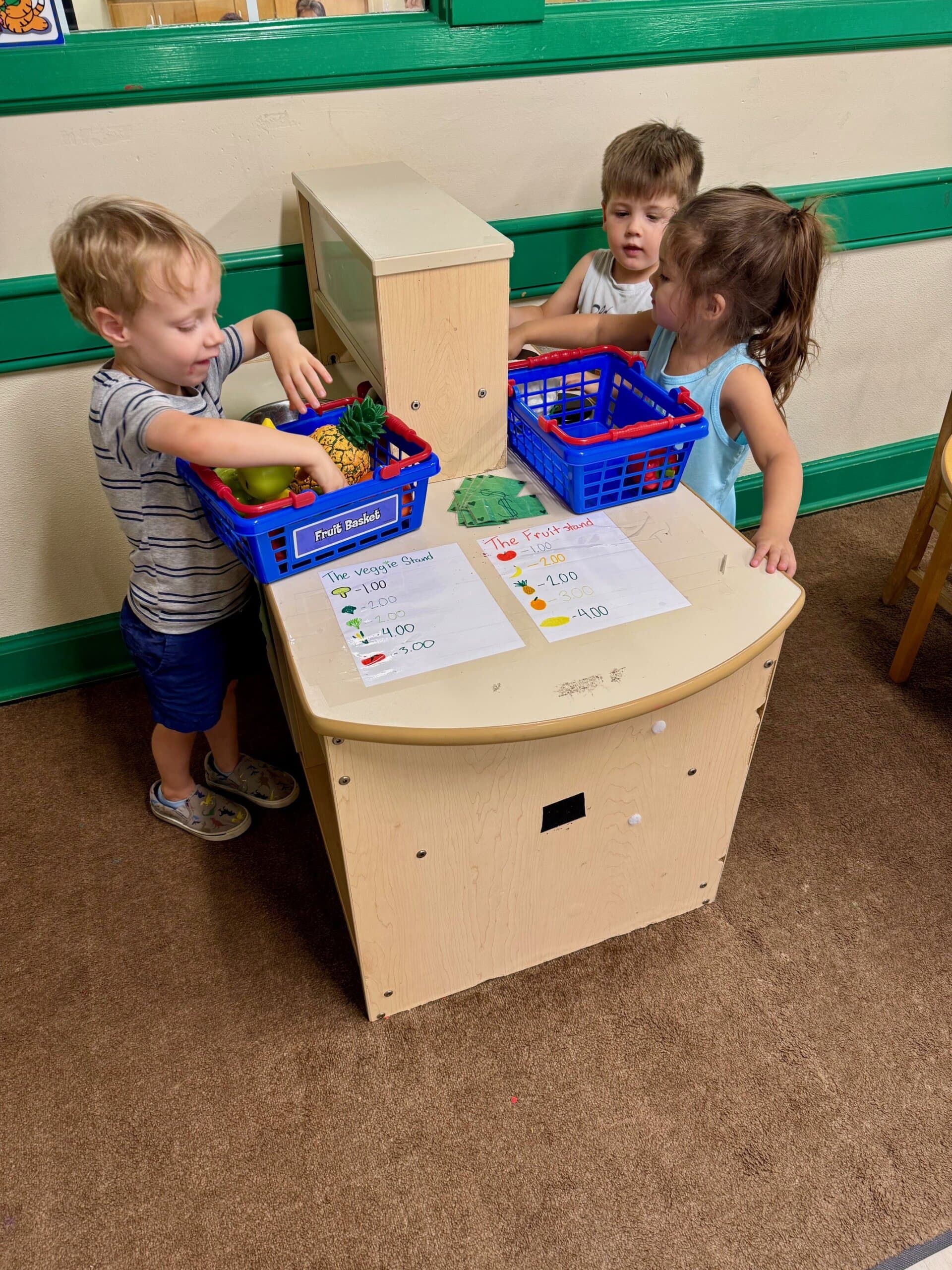 Preschool children engaging in dramatic play at the kitchen set, pretending to cook and serve food, encouraging imagination, collaboration, and social-emotional development