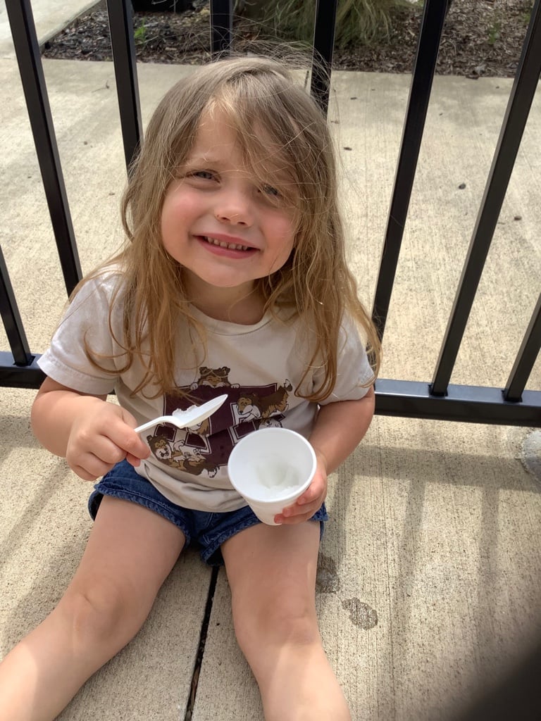little girl sitting outside smiling with a snowcone