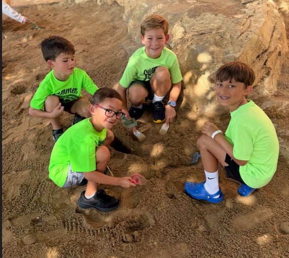 School aged boys on a field trip participating in a Dino Dig activity wearing a Summer Explorers school shirt 