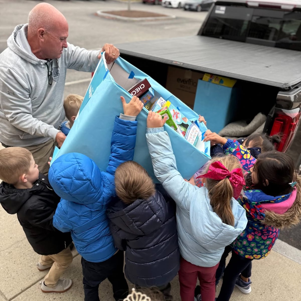 Primrose Burlington kindergarten students helping Burlington Police Officer David McLean load holiday gift donations for the Stuff a Cruiser community drive
