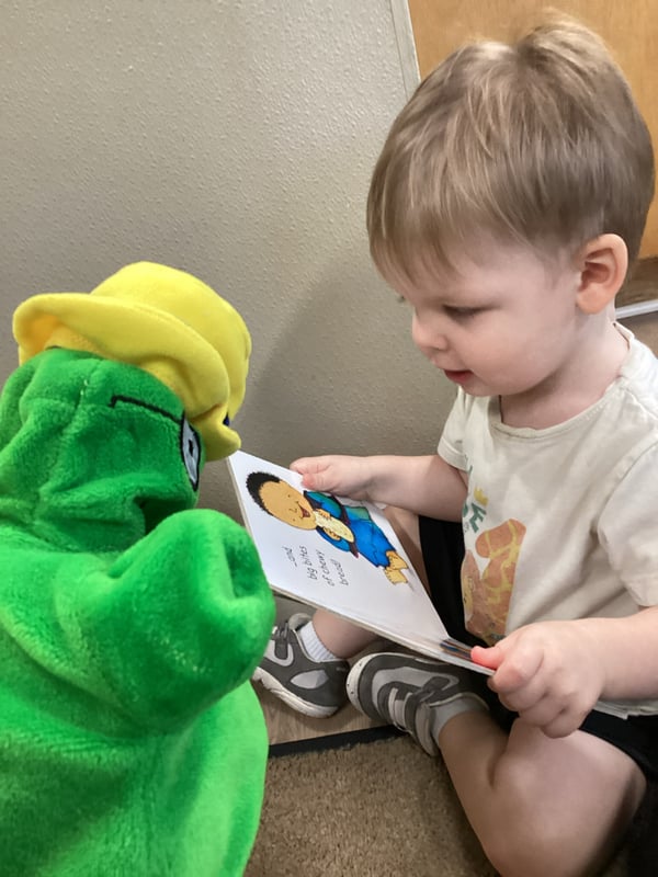 Infant reading a book with Primrose Puppet Og at Primrose School North Lewisville Lewisville TX
