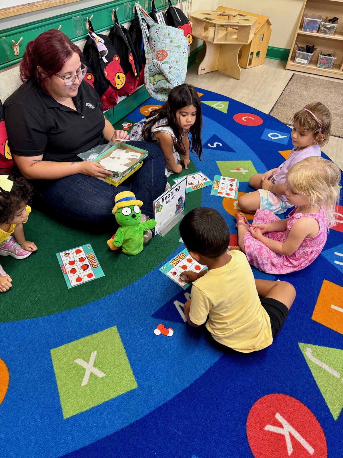Preschool aged students playing bingo with their teachers, using letter and word cards to build early literacy skills through interactive and fun group learning