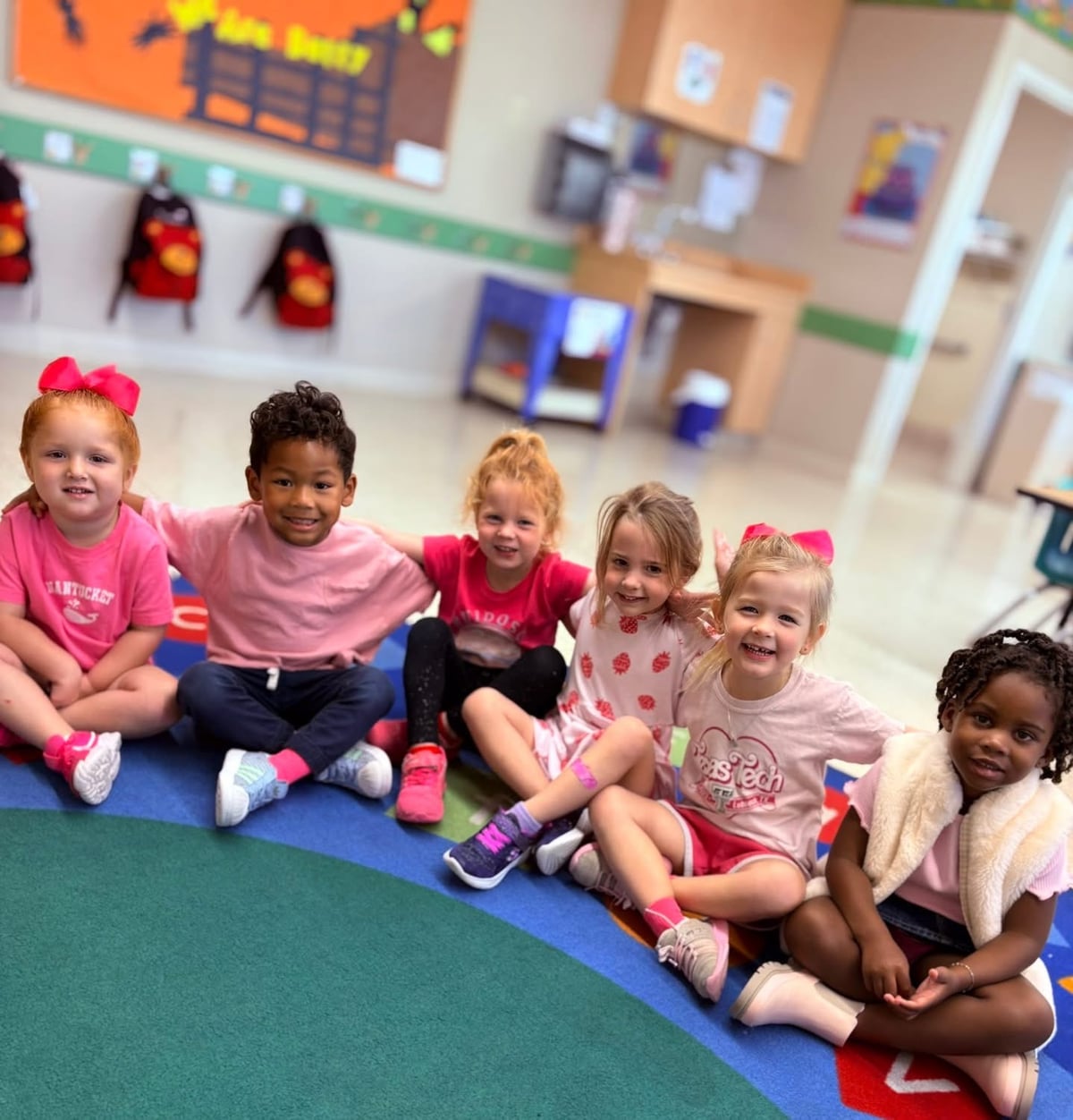 Preschool children sitting in a line with arms around each other wearing the color pink
