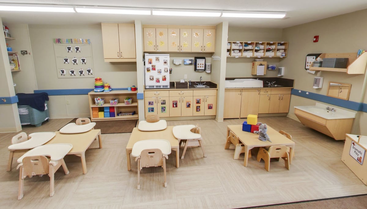 Primrose School of Eagan toddler classroom featuring age-appropriate tables and chairs, a dramatic play area, hands-on learning materials, dedicated diapering station, and child artwork displayed on the walls.