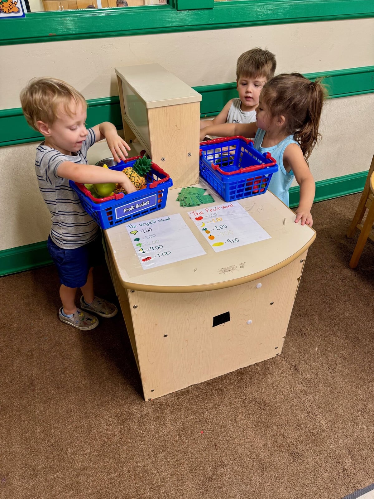 Preschool children engaging in dramatic play at the kitchen set, pretending to cook and serve food, encouraging imagination, collaboration, and social-emotional development