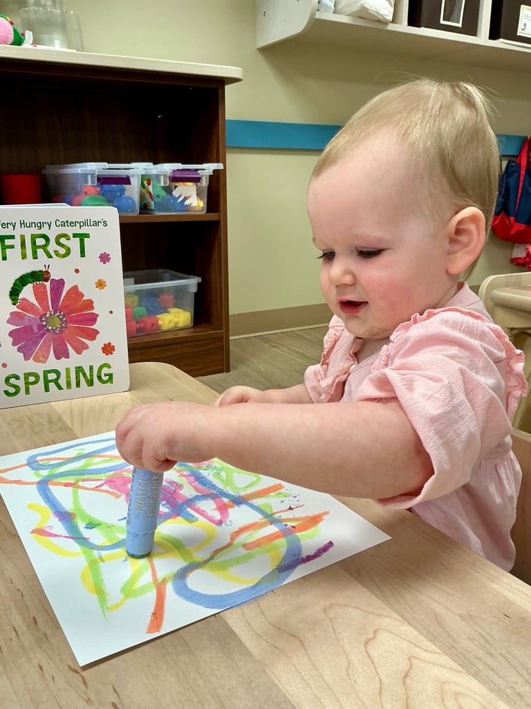Toddler creating colorful artwork in a Primrose School of Forest Hill classroom during a spring-themed learning activity.
