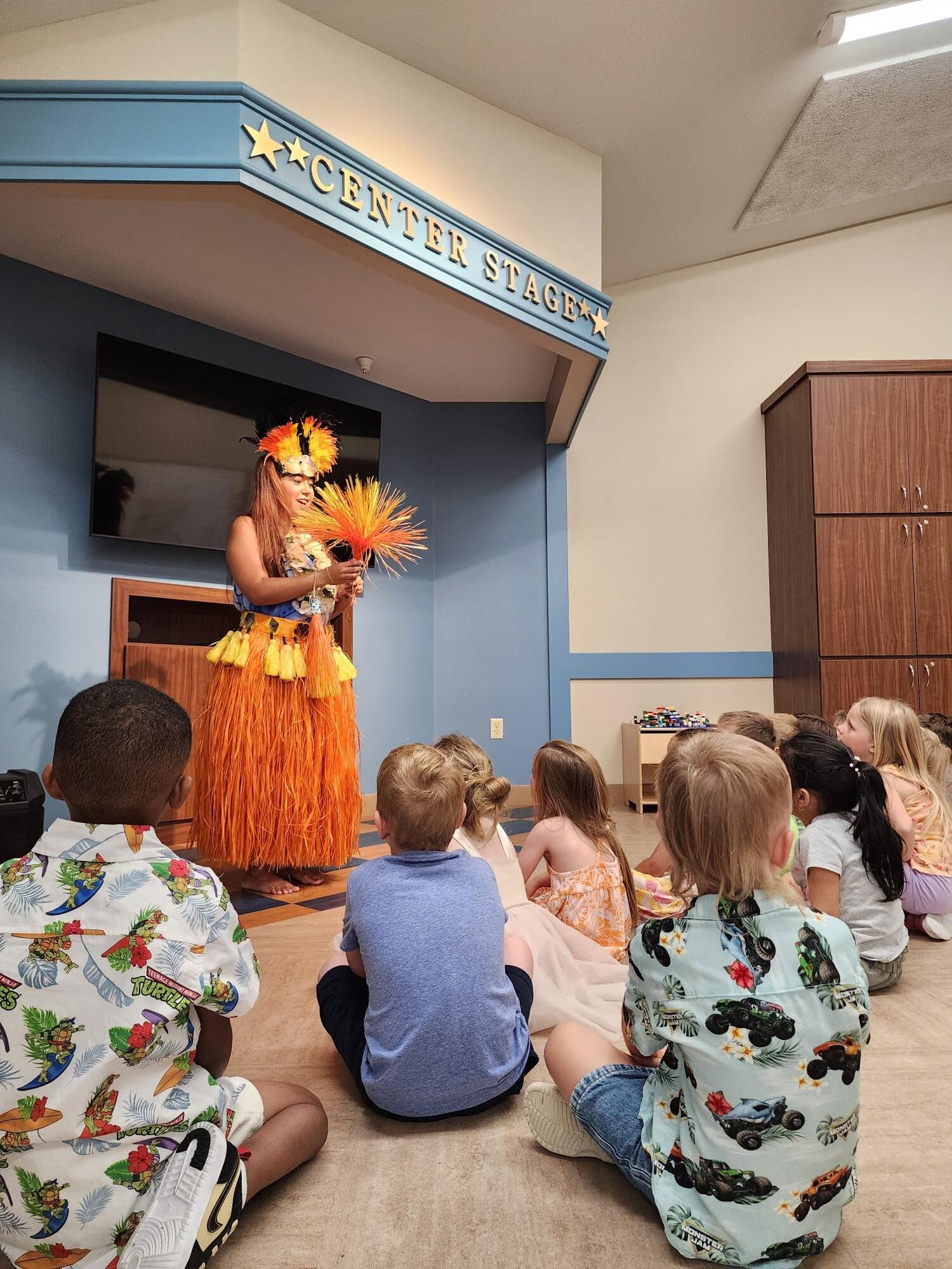 children seated together to watch a hula dancer perform while learning about Hawaiian culture through dance and storytelling