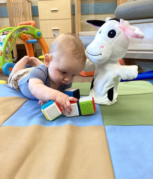 Adorable baby enjoying tummy time with colorful sensory cubes and a friendly cow puppet — perfect for boosting fine motor skills and early learning in North Fort Worth