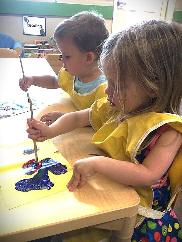 Toddlers exploring paint at a table using paint brushes. wonder time , painting , sensory play, educational childcare