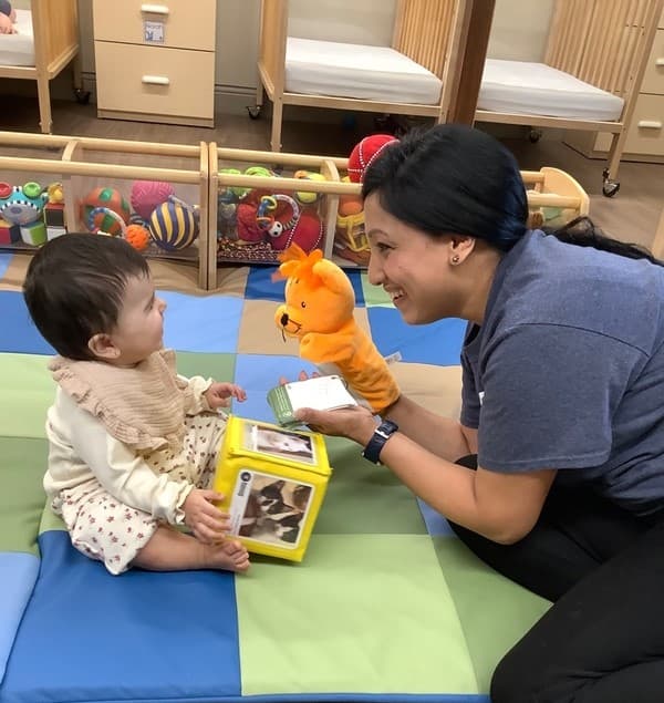 Primrose Fort Worth infant teacher engaging baby with a puppet and soft learning cube during sensory playtime. Haslet, TX, early child care