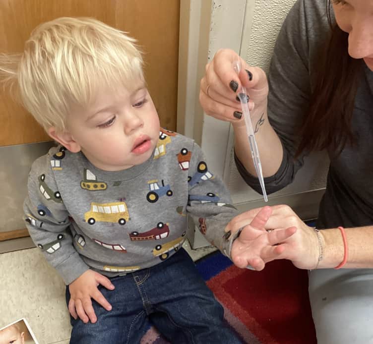 Toddler using an eyedropper with a teacher during a water exploration activity at Primrose School of Thornton