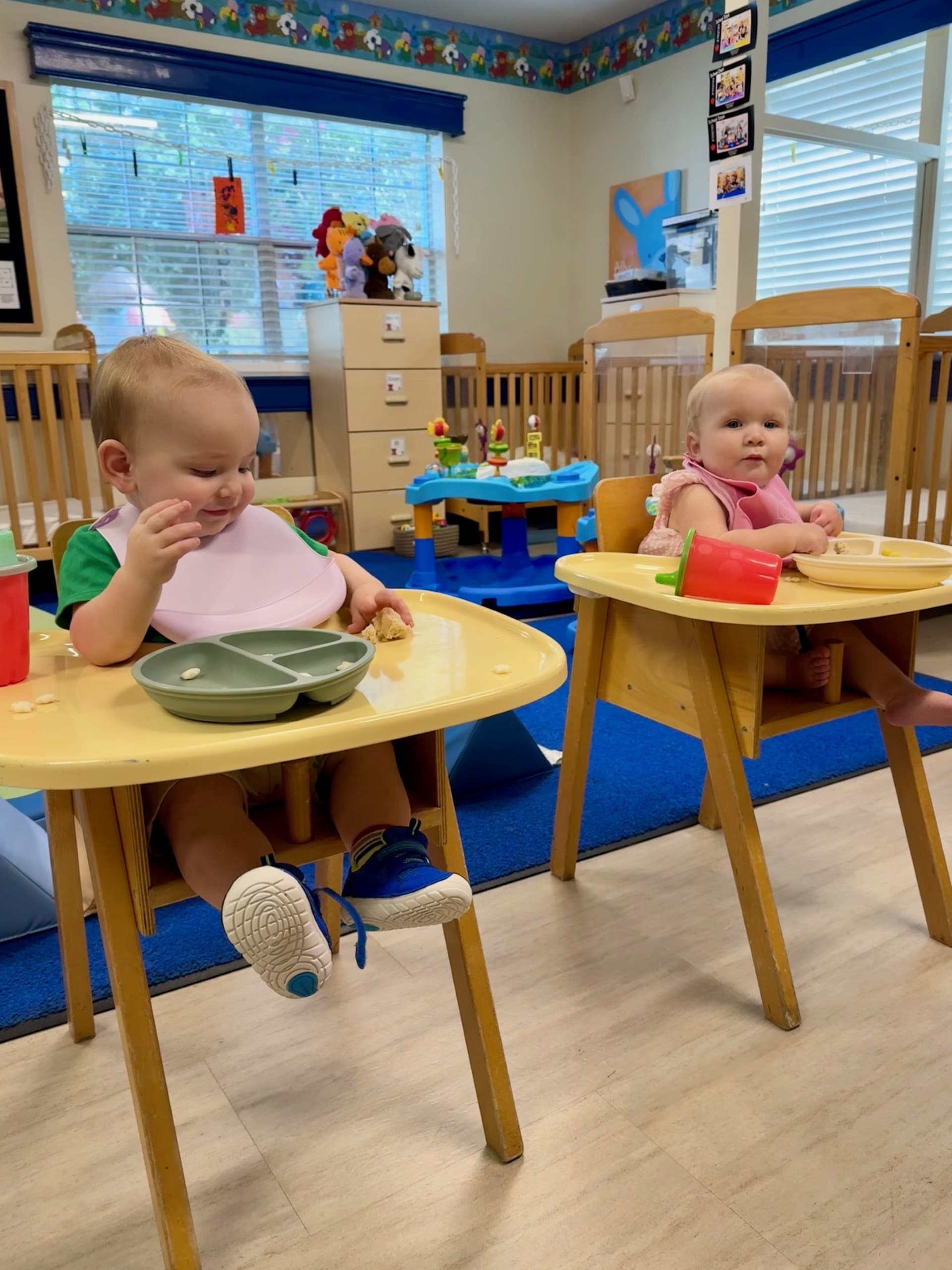 Infants sitting in low chairs independently eating finger foods, developing self-feeding skills and motor coordination