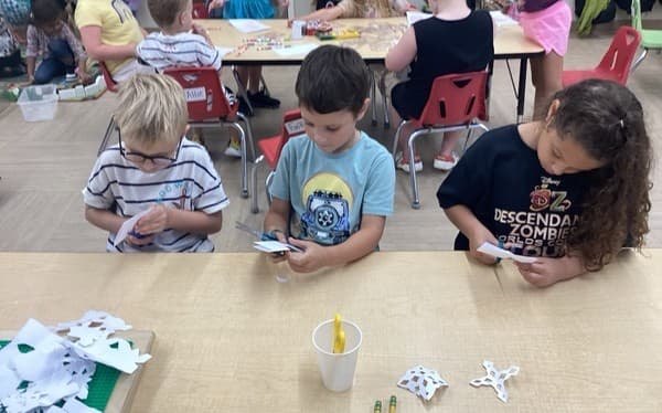 Children sitting down at a table cutting with scissors