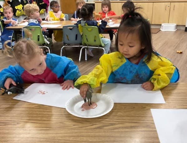 2 children dipping the feet of an animal figurine into paint and placing it on paper.