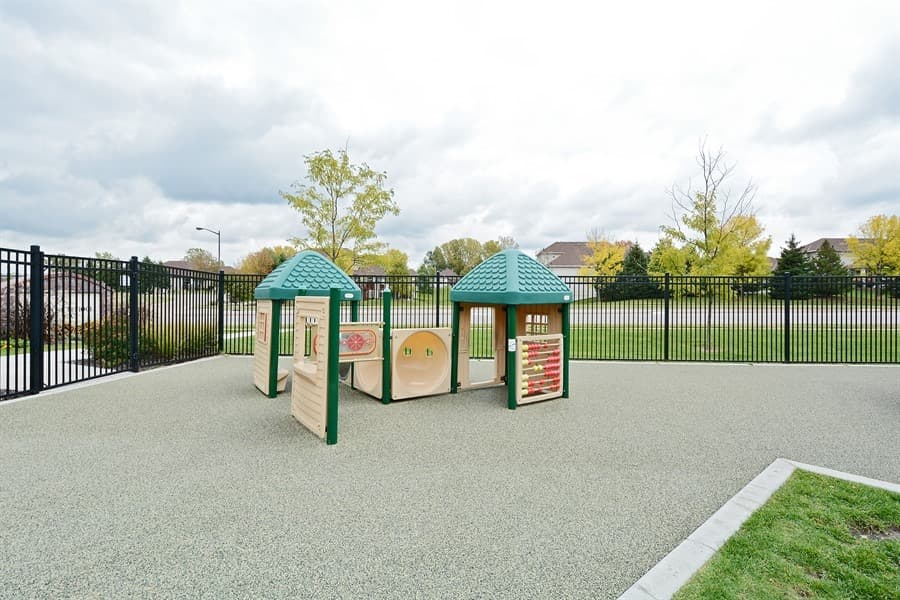 Early Preschool outdoor play area at Primrose School of Eagan featuring double play structures with green roofs, interactive activity panels, and rubber safety surfacing within a secure black iron fence