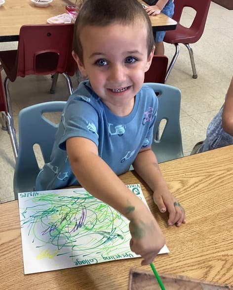 Preschool student proudly showing off a colorful painting project while developing creativity and fine motor skills through art exploration.
