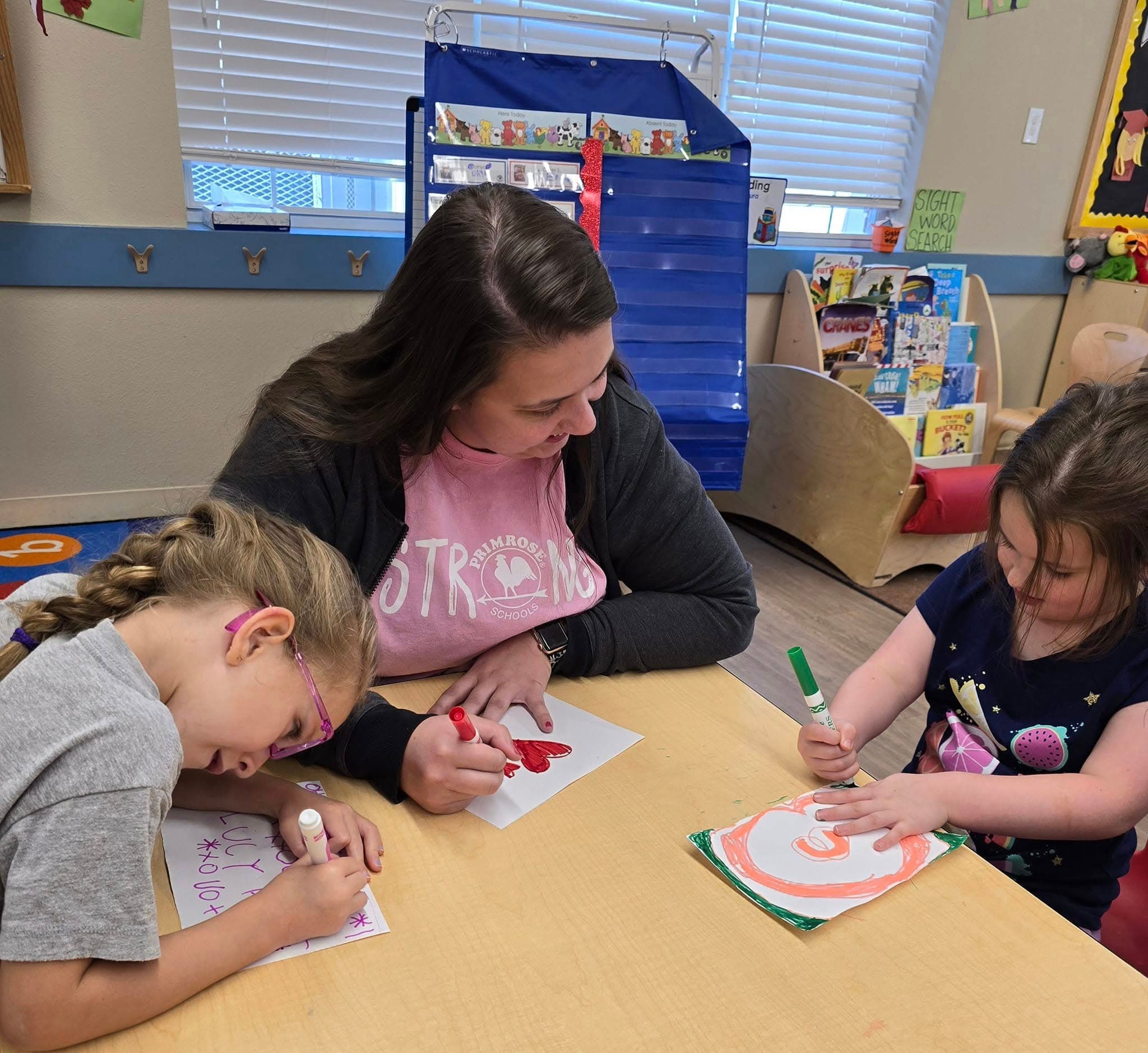 Preschool teacher guiding two young girls during an arts and crafts activity at a Fort Worth preschool classroom"