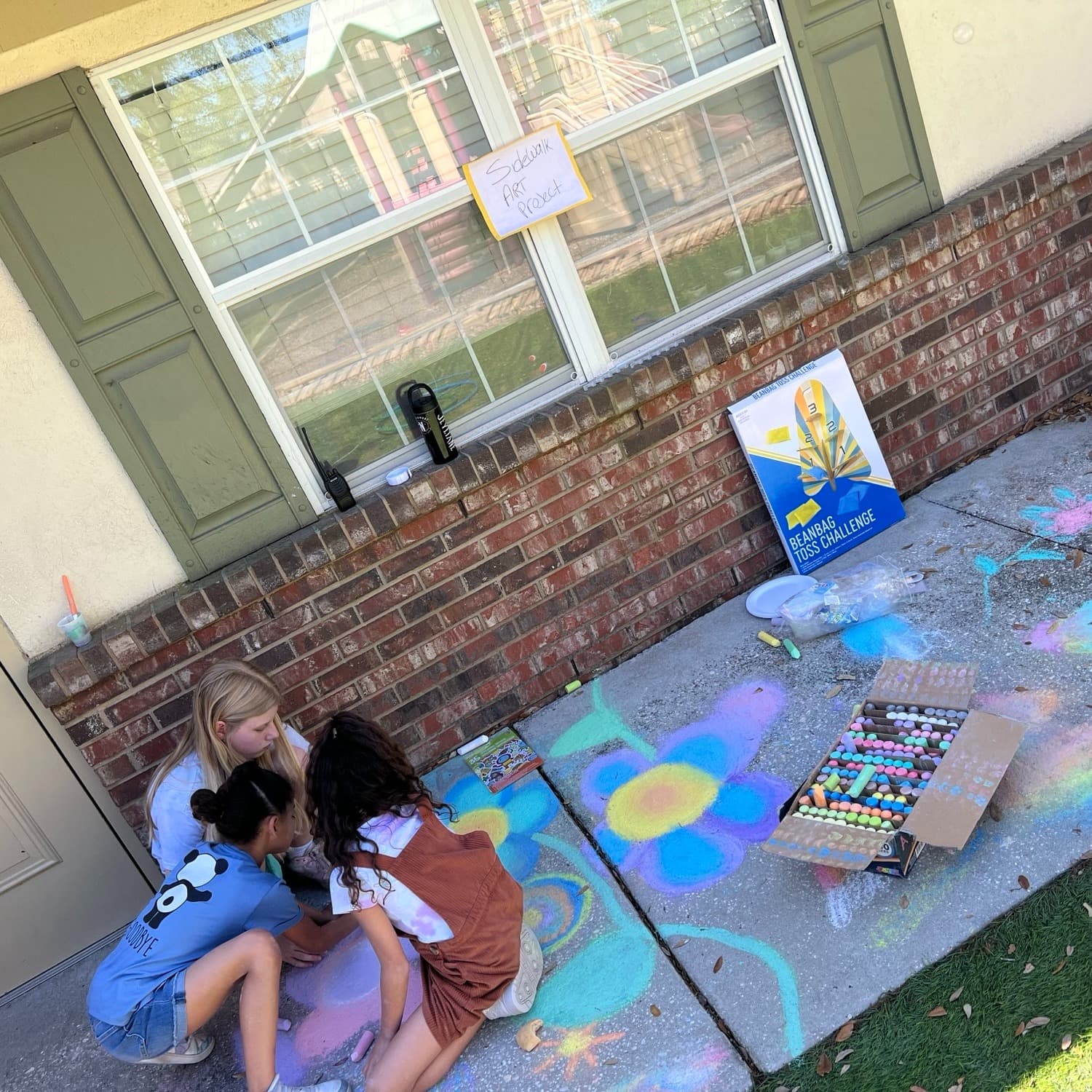 Children working together to create colorful sidewalk chalk art during an outdoor creative expression activity.