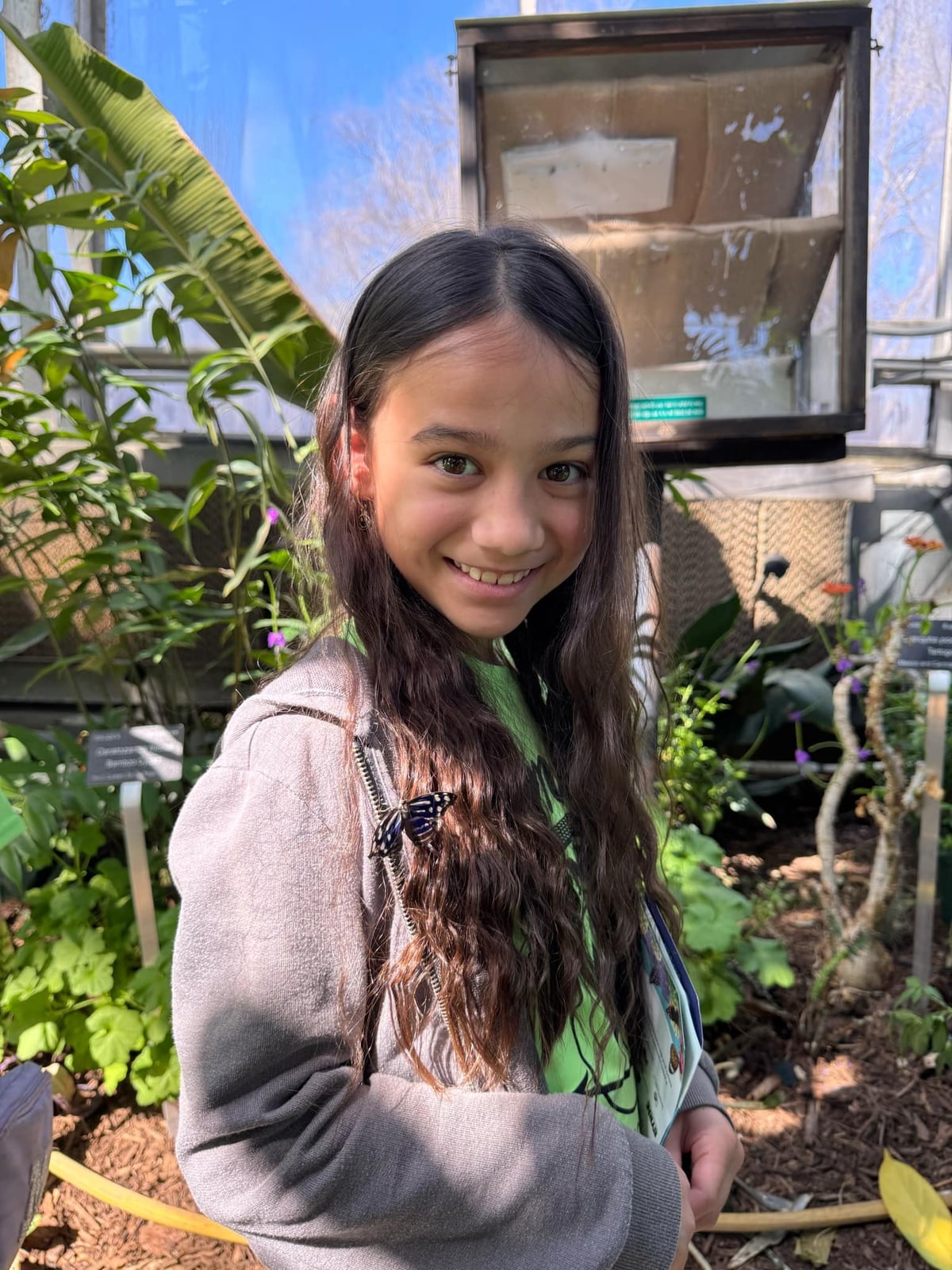 Happy preschool girl posing in a greenhouse, surrounded by vibrant foliage at the best afterschool care in Keller, TX.