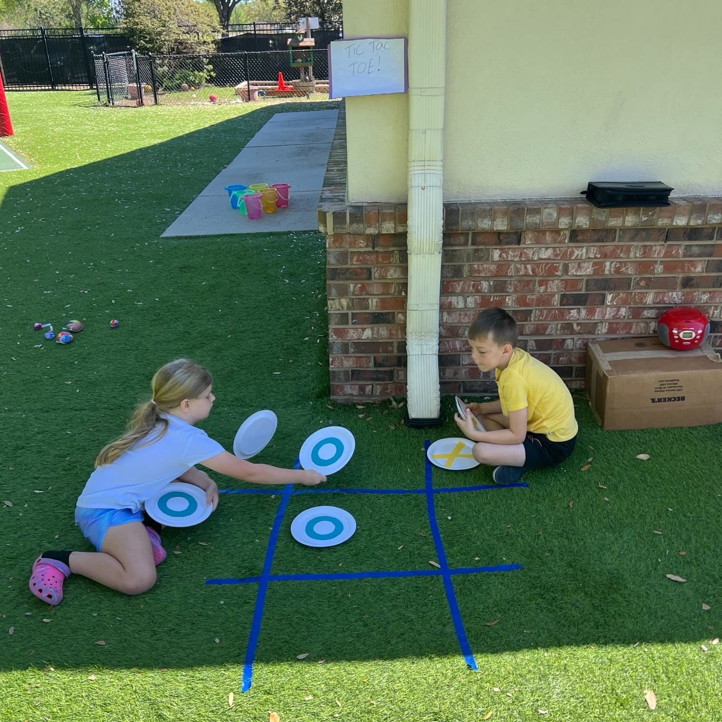 Children playing a life-sized tic-tac-toe game outdoors, building critical thinking, strategy, and social skills through interactive play.