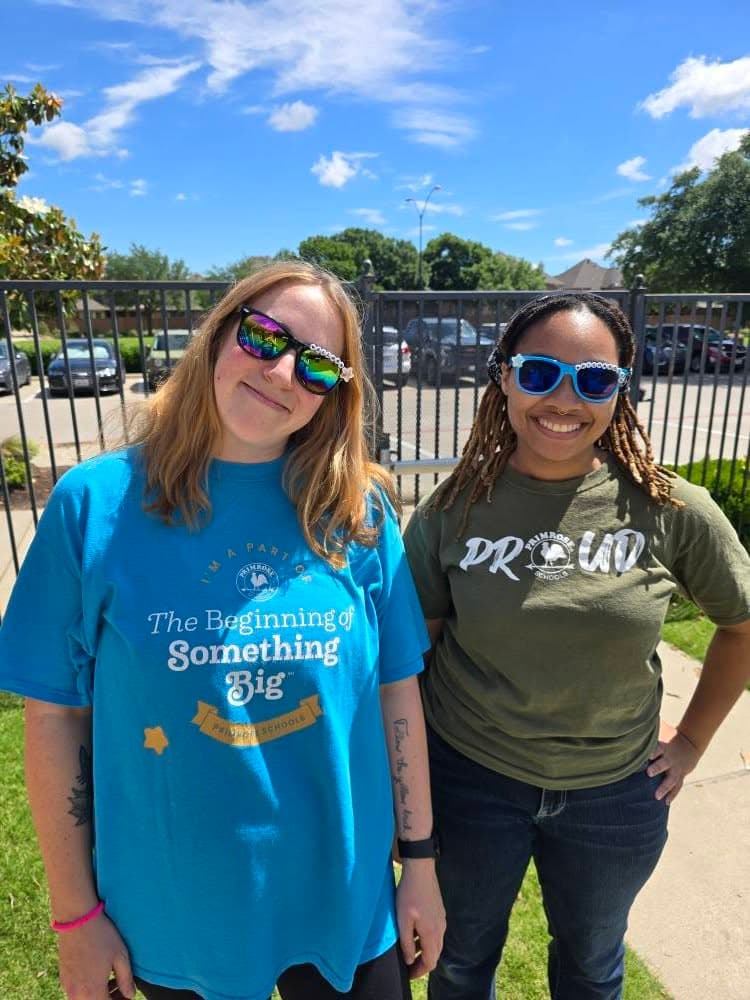 Two smiling staff wearing sunglasses and school tees at outdoor school event, modeling school spirit and community engagement