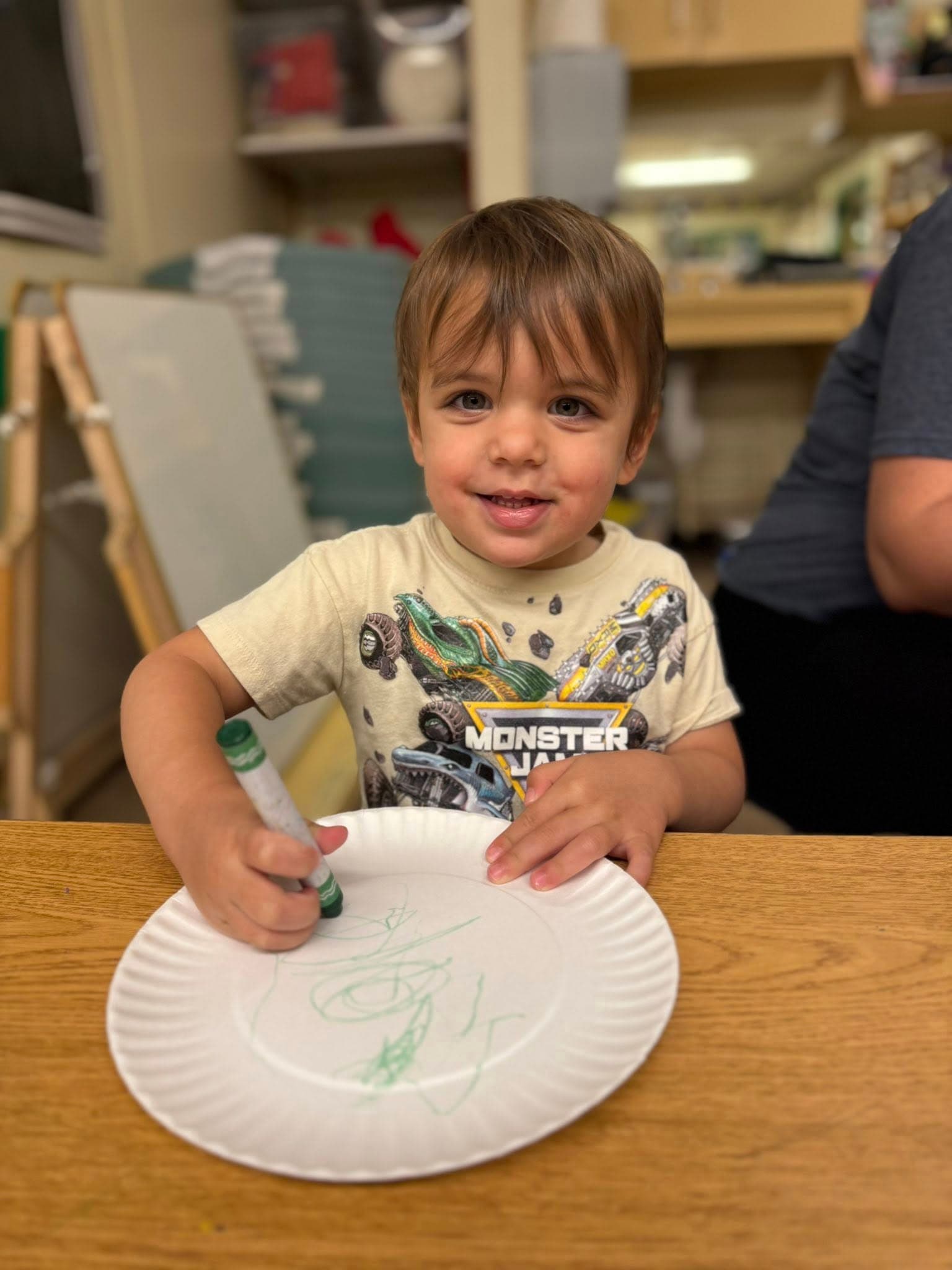 Preschool student practicing early writing and drawing skills with crayons during a creative classroom learning activity.