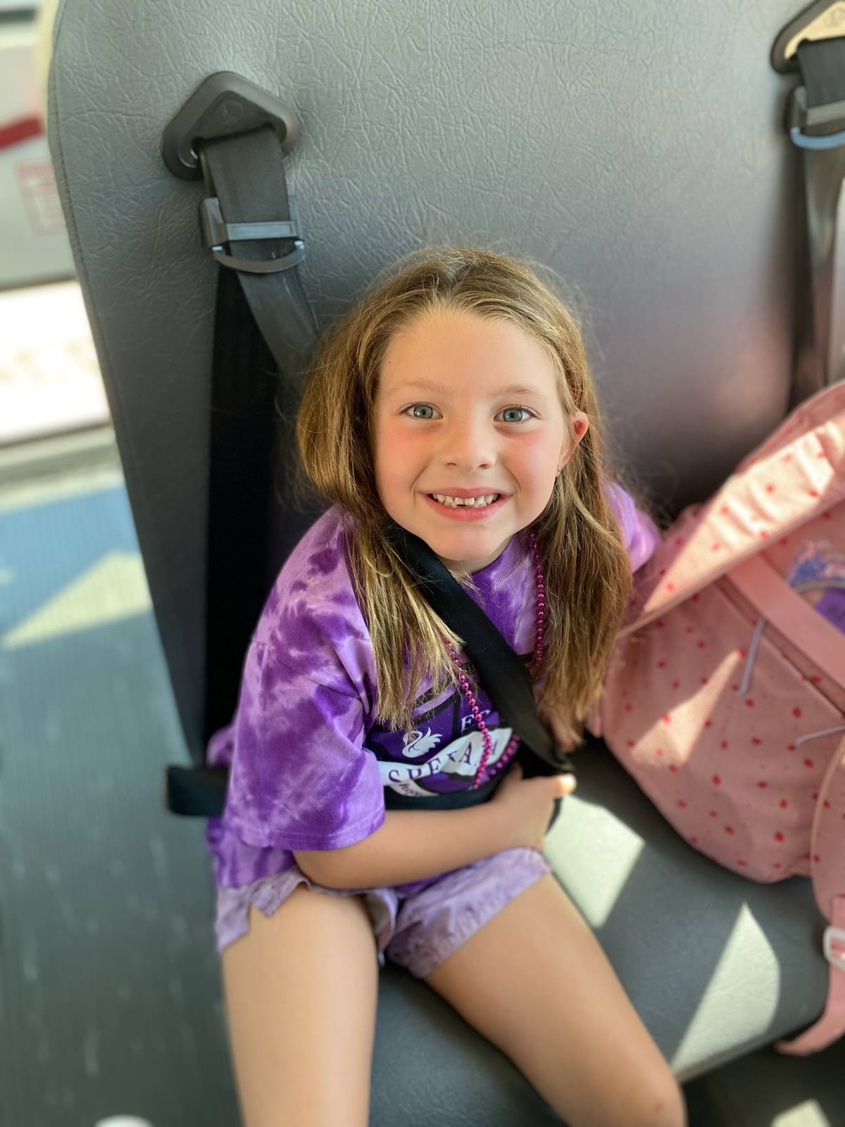 A Primrose School Explorer student in Keller, Texas smiling and riding the school bus safely with seat belt buckled