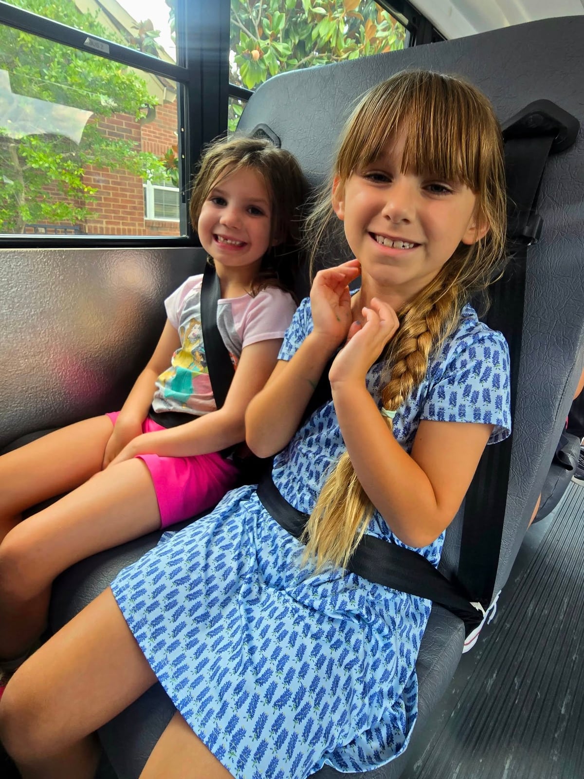 Two Primrose School Explorer students in Fort Worth, Texas smiling and riding the school bus safely with seat belts