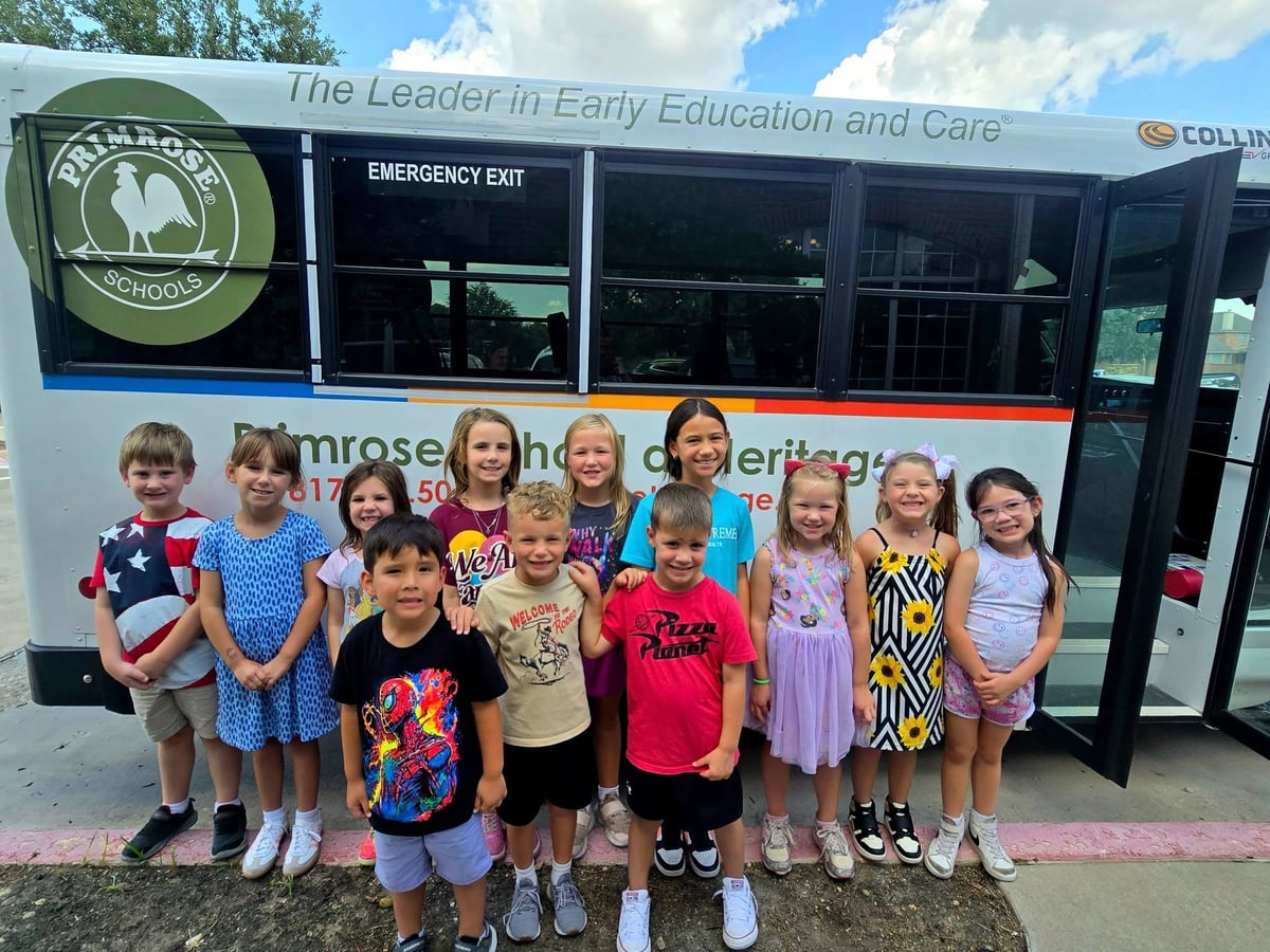 Primrose School Explorer students in Keller, Texas smiling in front of a school bus on the first week of school