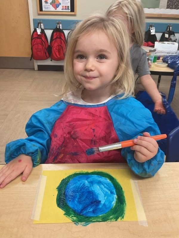 Preschooler painting a colorful artwork with a paintbrush during a classroom art activity that encourages creativity, self-expression, and fine motor development at Primrose School.