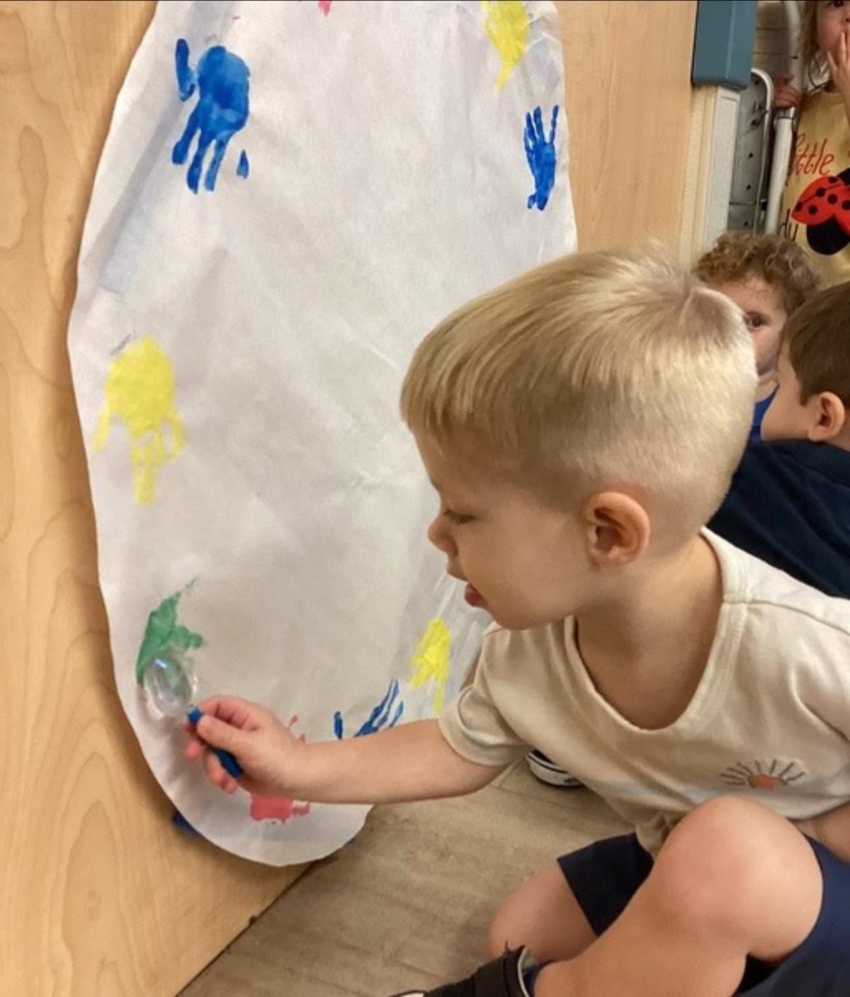 Toddler using a paintbrush to create colorful artwork on an easel during a classroom art activity that encourages creativity and fine motor development at Primrose School.