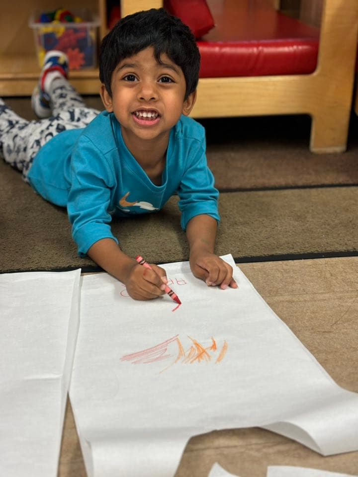 Young child drawing on large paper with crayons while developing pre-writing skills, creativity, and self-expression.
