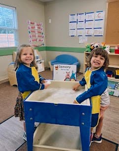 Two smiling children playing in the sensory bin during center time in a preschool classroom at Primrose School at Heritage.