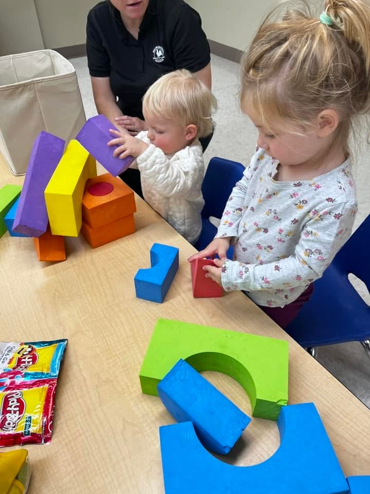 Toddlers stacking colorful foam blocks during a collaborative classroom activity that encourages problem-solving, spatial awareness, teamwork, and fine motor development at Primrose School.